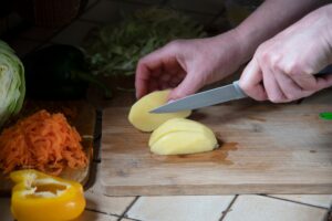 a woman cuts potatoes in the kitchen against the background of fresh vegetables,ingredients for soup